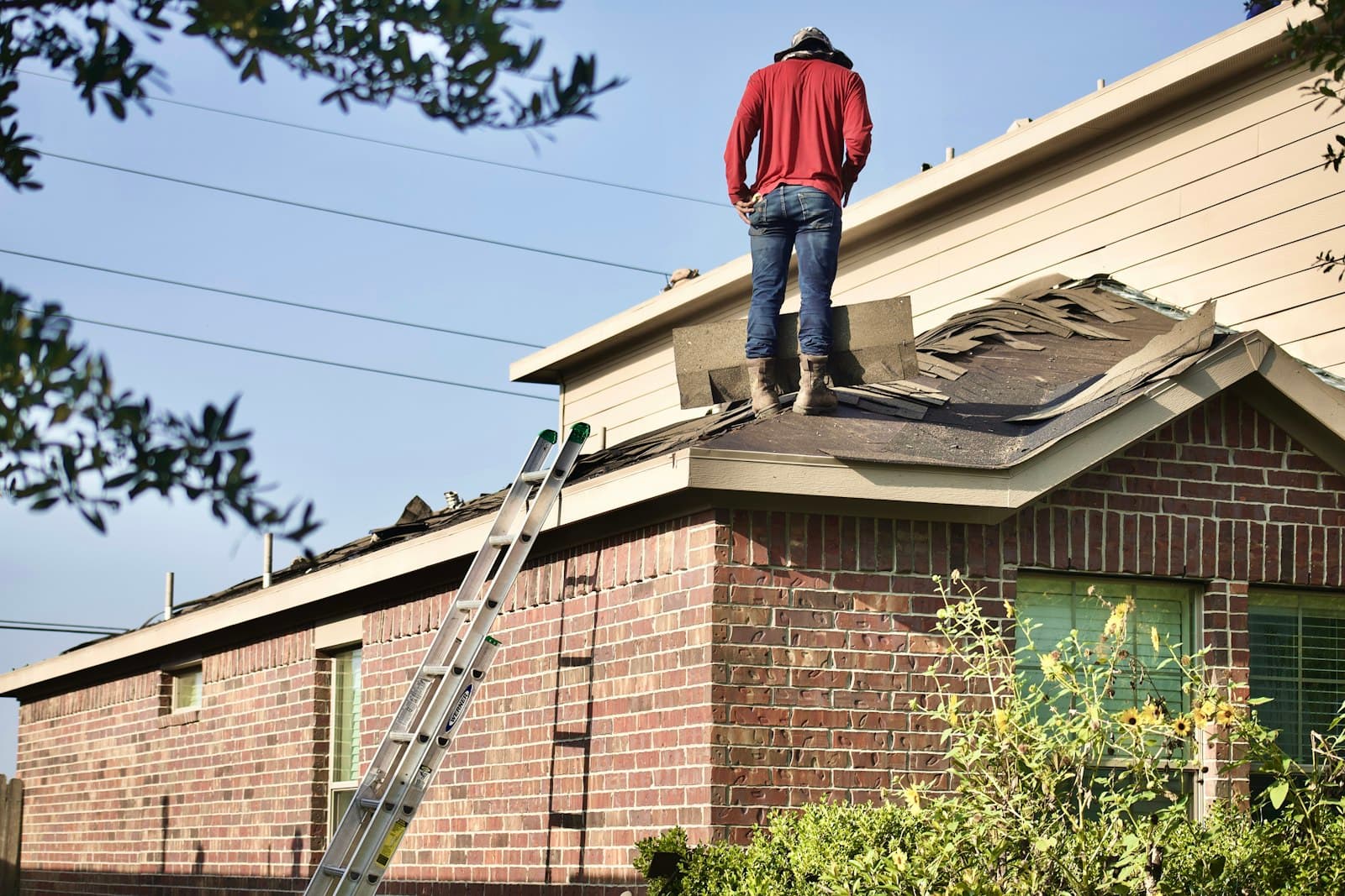 A roofer in a safety harness fastening architectural shingles
